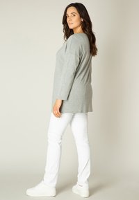 Graues Langarmshirt mit lockerem Schnitt, seitlichen Schlitzen, kombiniert mit weißen Jeans und weißen Sneakers. Glatte Stofftextur mit Rundhalsausschnitt.