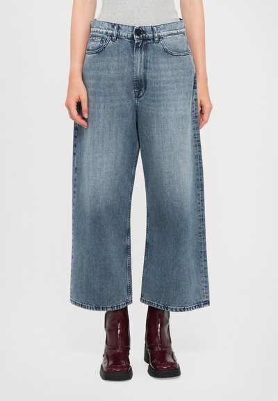 Löysät siniset denim-farkut, joissa on keskikorkea vyötärö, viisi taskua ja rento malli, yhdistettynä burgundinpunaisiin korotettuihin nilkkabootseihin.