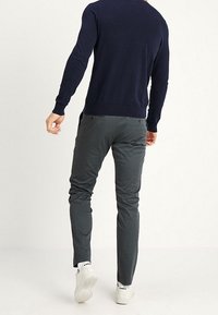 Marinblå tröja med långa ärmar, figurnära design; grå byxor med smal passform; bärs med vita sneakers. Sedd bakifrån.