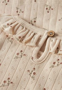 Roomkleurige geribbelde stof met kleine bruine bloemenprint, voorzien van een gerimpelde halslijn en een enkele ronde houten knooplus sluiting.