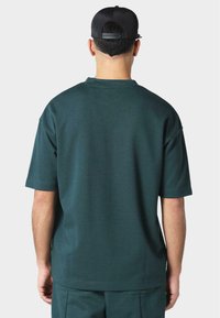 Sötét türkiz, oversized póló rövid ujjakkal, kerek nyakkivágással és sima tapintással, egyszínű, hozzáillő nadrággal párosítva.
