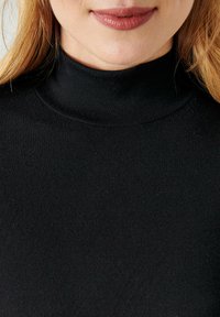 Dolcevita nero realizzato in tessuto morbido e elastico. Dettaglio ravvicinato che mette in evidenza una superficie liscia e una vestibilità aderente attorno al collo e alle spalle.