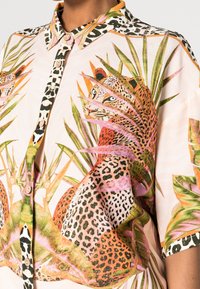 Chemise à manches courtes imprimée avec un fond rose orné de motifs léopard et feuillages, devant à boutons et col pointu.