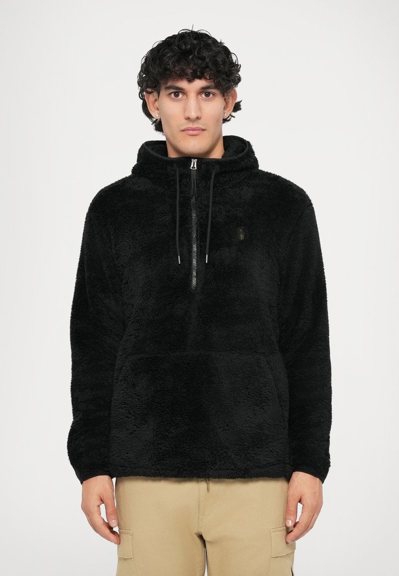 Pulover negru din fleece, cu guler înalt, fermoar în față și șnur de strângere. Prezintă un material moale, texturat și un accent subtil cu logo-ul brandului.