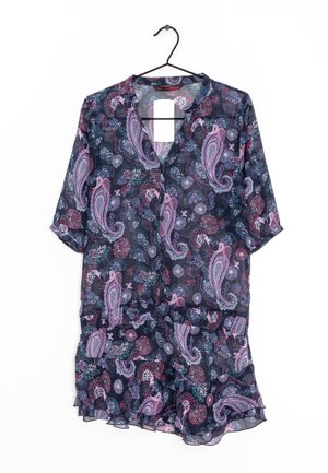 Blusa oscura con estampado floral y paisley en rosa y teal, con diseño de botones y manga corta, colgada en un perchero negro.