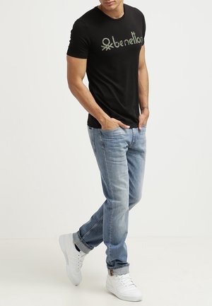Sort bomulds T-shirt med "benetton" logo i camouflage stil, parret med lyseblå denim jeans og hvide sneakers.