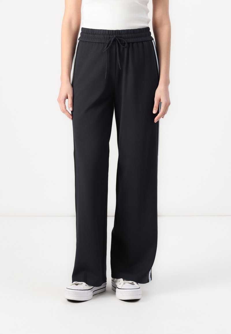 Sorte sweatpants med bred benåbning, elastisk talje og snor, med hvide sidestriber og lige snit, lavet af blødt materiale.
