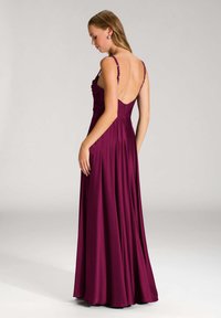 Lungo abito da sera bordeaux con profondo scollo a V sulla schiena, corpetto arricciato e sottili spalline decorate. Tessuto liscio, simile alla satinato, con una silhouette fluida.