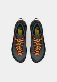 Sapatos de exterior em cinza e preto com um upper feito de material texturizado, apresentando atacadores laranja brilhante e um design de sola robusto.