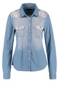 Chemise en denim bleu clair à manches longues, avec des accents en dentelle aux épaules, deux poches poitrine et un boutonnage sur le devant. Texture légèrement décolorée.