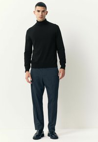 Crna turtleneck džemper i prugaste sive hlače, sa slim fit dizajnom. Glatka tekstura sa rebrastim manžetama i rubovima. Crne cipele.