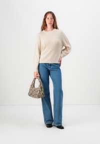 Un pull beige à côtes, un jean flare bleu et un sac à main beige à motif serpent. Les chaussures présentent un design à bout pointu.
