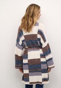 Pletený cardigan s patchworkovým dizajnom v krémovej, hnedej, modrej a levandulovej farbe. Má dlhé rukávy, opasok v páse a textúrovanú tkaninu.