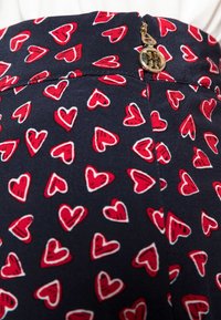Falda azul marino con un patrón de corazones rojos con contornos blancos, cierre de cremallera y un acento de hardware dorado. Textura de tela suave.