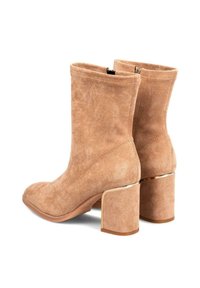 Par de botines de ante color beige con tacones de bloque, cremalleras laterales y delgados acentos metálicos sobre los tacones, sobre un fondo blanco.