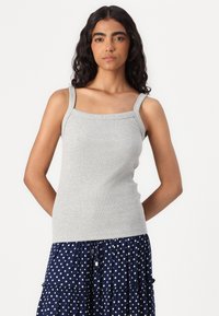 Grå, ribbet tanktop med brede stropper og firkantet halsutskjæring. Kombinert med en marineblå, prikkete, lagdelt skjørt. Glatt tekstur, figurnær design.