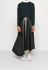 Tmavě zelený pletený svetr, černá kožená midi sukně, bílé tenisky a černá taška. Hladké textury, zaoblený výstřih a pohodlný střih.