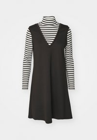 Vestido negro sin mangas con escote en V, superpuesto sobre una camiseta de rayas en blanco y negro de manga larga. Tejido de algodón, corte holgado, rayas verticales.