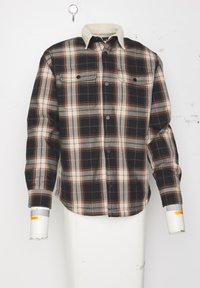 Geruite shirt met zwart, bruin, grijs en wit. Zachte beige kraag, twee borstzakken en zwarte knopen; lange mouwen met manchetten.