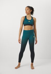Reggiseno sportivo e leggings in gradiente turchese e nero, con dettagli in logo dorato, tessuto morbido e design aderente.