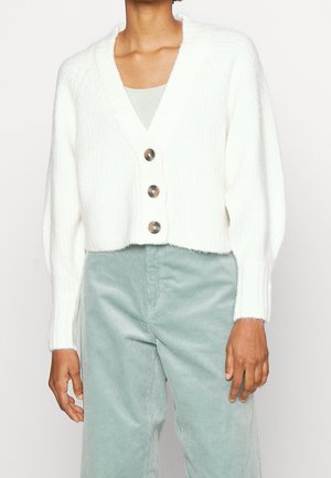 White ribbed knit cardigan with three large buttons worn over a light gray top, paired with high-waisted light green corduroy pants.
