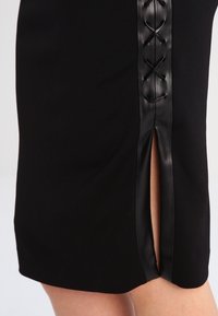 Falda negra con una abertura lateral y detalles de cordones de cuero sintético negro. Tela suave con una silueta ajustada, adecuada para varias ocasiones.