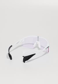 Ochelari de soare sportivi cu ramă albă, lentile ușor colorate în roz și accente negre. Designul include vârfuri sportive pentru confort.