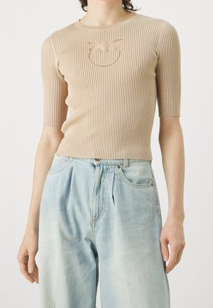 Beige geribd kortärmelig topje met een subtiel kattengezicht patroon gecombineerd met hooggetailleerde lichtblauwe wijde spijkerbroek.