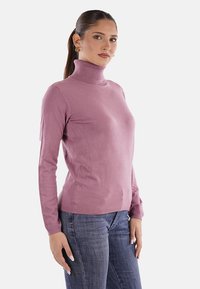 Maglione a collo alto rosa chiaro, design aderente, maniche lunghe, colletto e orlo a costine, realizzato in un materiale morbido, abbinato a jeans blu.