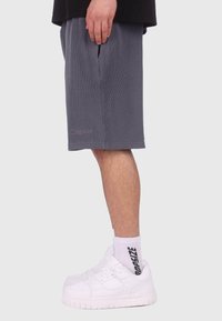 Grau gestreifte Shorts aus Cord mit Seitentaschen, aus strukturiertem Stoff. Kombiniert mit weißen Sneakern und Socken mit schwarzem Schriftzug.