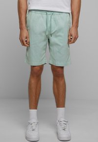 Shorts vert menthe clair avec une taille élastique, un cordon de serrage et des poches latérales, fabriqués dans un tissu doux. Portés avec des baskets blanches.