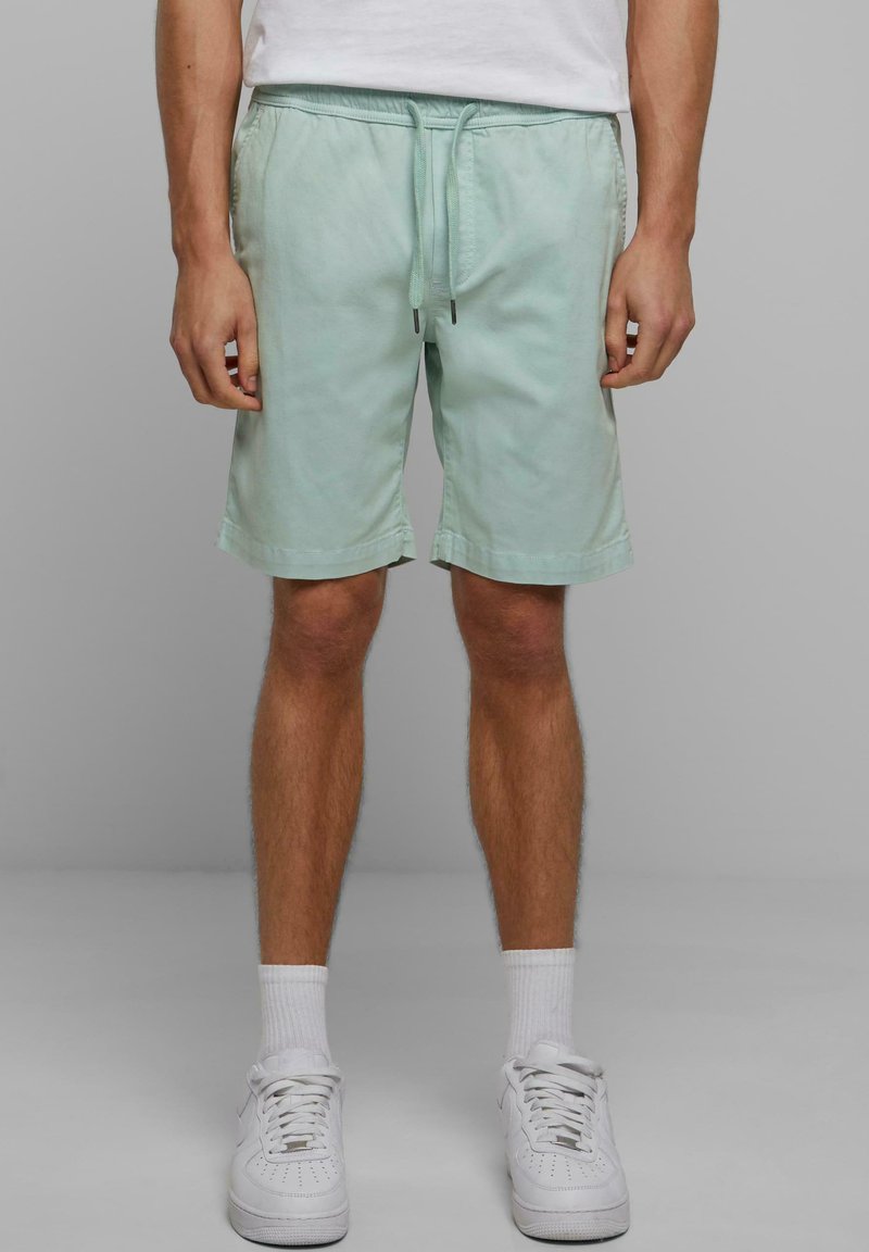 Shorts vert menthe clair avec une taille élastique, un cordon de serrage et des poches latérales, fabriqués dans un tissu doux. Portés avec des baskets blanches.