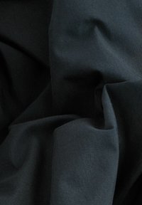 Crni materijal s glatkom teksturom, s blago naborima i naborima, prikazuje jedinstvenu boju bez uzoraka ili značajnih ukrasa.