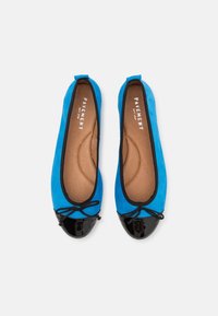 Paire de ballerines bleues avec bouts noirs vernis, bordure noire, petits détails de nœuds et semelles intérieures beiges rembourrées étiquetées « Pavement ».