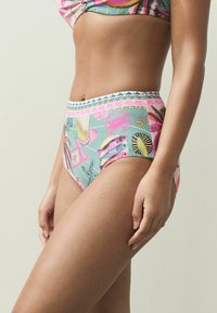 Augsta vidukļa bikini apakšdaļa krāsainā tropu rakstā. Tam ir gluda tekstūra, elastīgs viduklis ar dekoratīvu apdari un spilgtas rakstaina. 