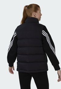 Zwarte puffer gilet met hoge kraag, voorzien van dikke gewatteerde secties en witte strepen op de mouwen. Zachte textuur en een relaxte pasvorm.