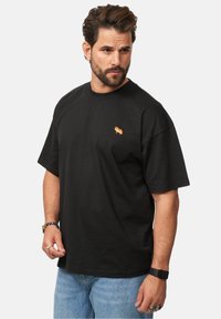 Black cotton t-shirt with short sleeves and a crew neck, featuring a small red and yellow embroidered design on the left chest.