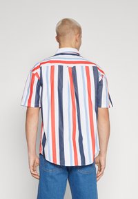 Camicia a maniche corte con colletto, caratterizzata da righe verticali in rosso, blu e bianco. Realizzata in cotone, con orlo dritto e una piega sul retro.