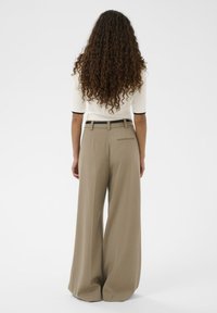 Pantaloni bej cu croială largă și design ajustat, prevăzuți cu curea și buzunar în spate, asortați cu un top alb cu mâneci scurte.