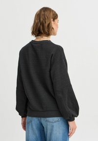 Felpa nera, strutturata, con spalle scese e maniche a sbuffo, abbinata a jeans chiari a gamba larga. Design semplice e casual.