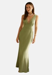 Langes, figurbetontes Kleid aus weichem olivgrünem Satin mit tiefem V-Ausschnitt und Spitzelementen. Verfügt über eine schicke Silhouette und einen leichten Schlag am Saum.