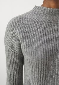 Maglione grigio lavorato a maglia con trama a coste, collo alto e silhouette aderente, che mette in mostra un materiale morbido e sottili linee verticali.
