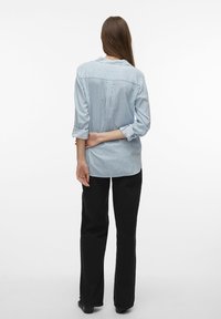 Camicetta a righe blu e bianche con maniche lunghe e orlo curvo, abbinata a pantaloni larghi neri. Entrambi i capi sono casual e sono caratterizzati da una vestibilità ampia.