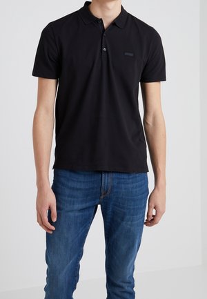 Sort poloshirt i bomuldsmateriale med klassisk krave, korte ærmer, enkelt knaplukning og en lille logo på brystet.