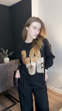 Svart sweatshirt med stora guldglittrande bokstäver "LOVE", kombinerad med lösa svarta byxor. Mjuk tygstruktur, avslappnad passform.