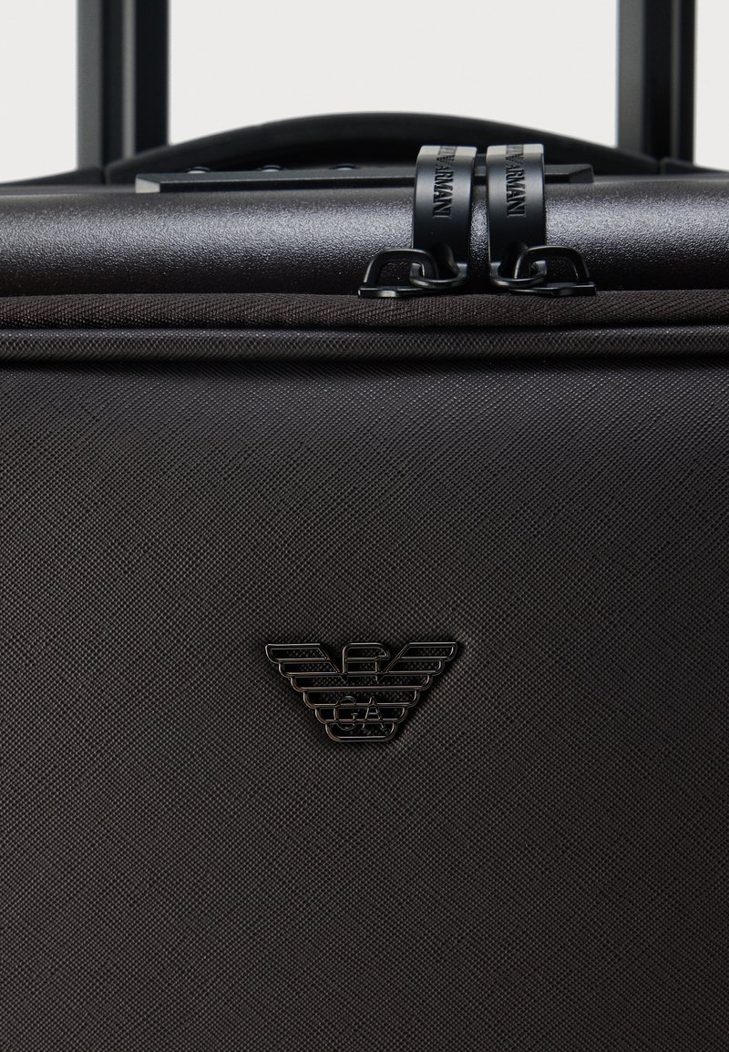 Black hard-shell suitcase with textured finish, prominent logo, dual zippers, and a retractable handle. Compact and rectangular design.