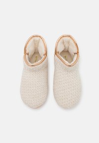 Cream-colored slippers with woven texture, fur lining, and a rose gold accent around the opening. Rounded toe and flat sole.