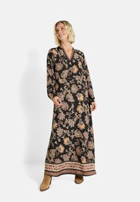 Robe longue noire avec des motifs floraux en crème et or. Col en V, manches longues et une finition décorative avec des rayures contrastées.