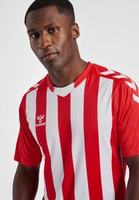 Rød og hvid stribet sportsjersey med korte ærmer og v-hals, der har Hummel-logoet på venstre bryst og skulderdetaljer.