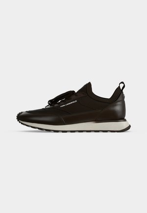 Μαύρο sneaker χαμηλού τύπου με λευκή σόλα, σχέδιο με κορδόνια και λογότυπο Karl Lagerfeld στο πλάι, πάνω σε απλό φωτεινό φόντο.